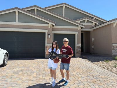 Happy couple holding a sold sign in front of their new house